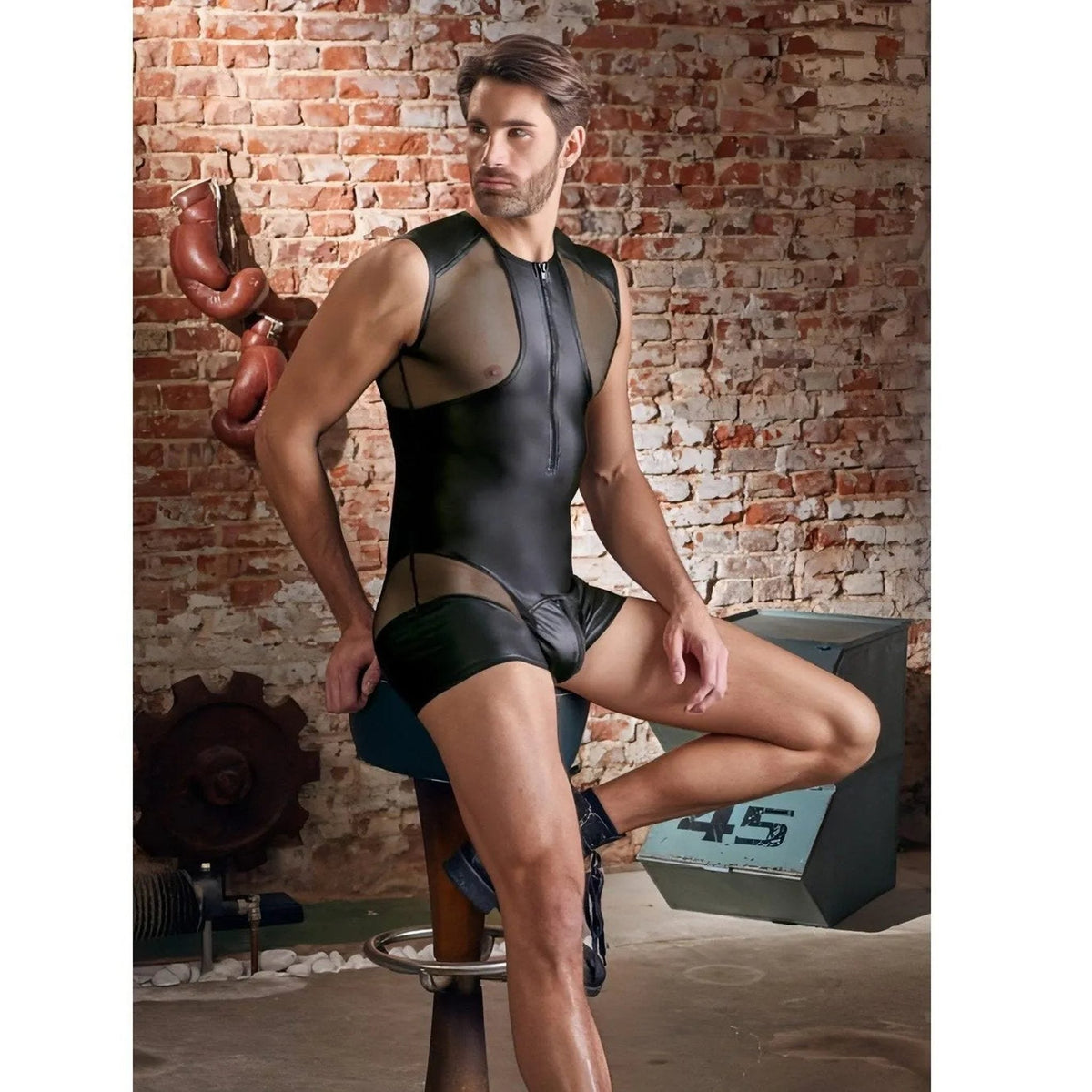 Playsuit uomo nero opaco seduto su sgabello con inserti rete e zip pubica