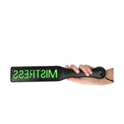 Mano femminile che impugna paddle BDSM nero con scritta verde neon