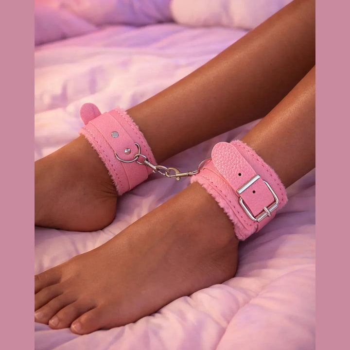 Cavigliere bondage rosa con orecchie in similpelle indossate su gambe sdraiate su letto rosa