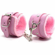 Cavigliere bondage rosa in similpelle con pelliccia, fibbie D-ring e catenella metallica su bianco
